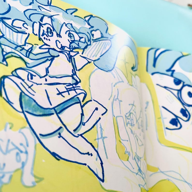 May include: A close-up of a sketchbook page with a vibrant yellow background. The page features a whimsical illustration in blue and white, depicting a cartoon character in motion. The artwork has a playful and energetic feel, with dynamic lines and expressive details.