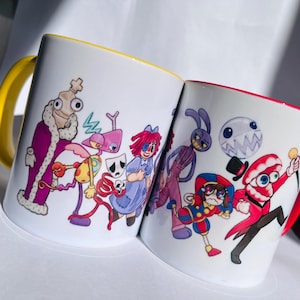 Puede incluir: Dos tazas de cerámica blanca con personajes de dibujos animados coloridos impresos en ellas. La taza de la izquierda tiene un borde amarillo y presenta personajes de colores morado, rojo, azul y amarillo. La taza de la derecha tiene un borde rojo y presenta personajes de colores rojo, azul, morado y blanco.