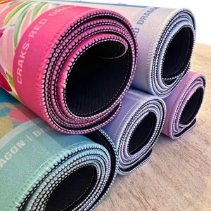 May include: Rolled-up mouse pads in various colors, including pink, blue, and purple. The pads have a black interior and white stitching around the edges. The text "CRAKS-RED DRAGON" is visible on one of the pads.