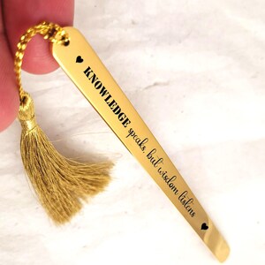 May include: Gold bookmark with a tassel. The bookmark has the quote "KNOWLEDGE speaks, but wisdom listens" engraved on it.