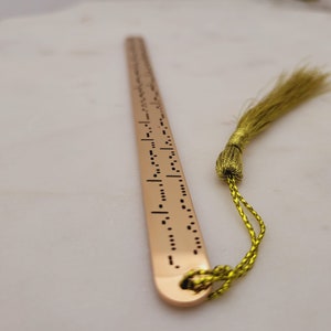 May include: A gold bookmark with a tassel. The bookmark has a pattern of dots and dashes, which is braille.