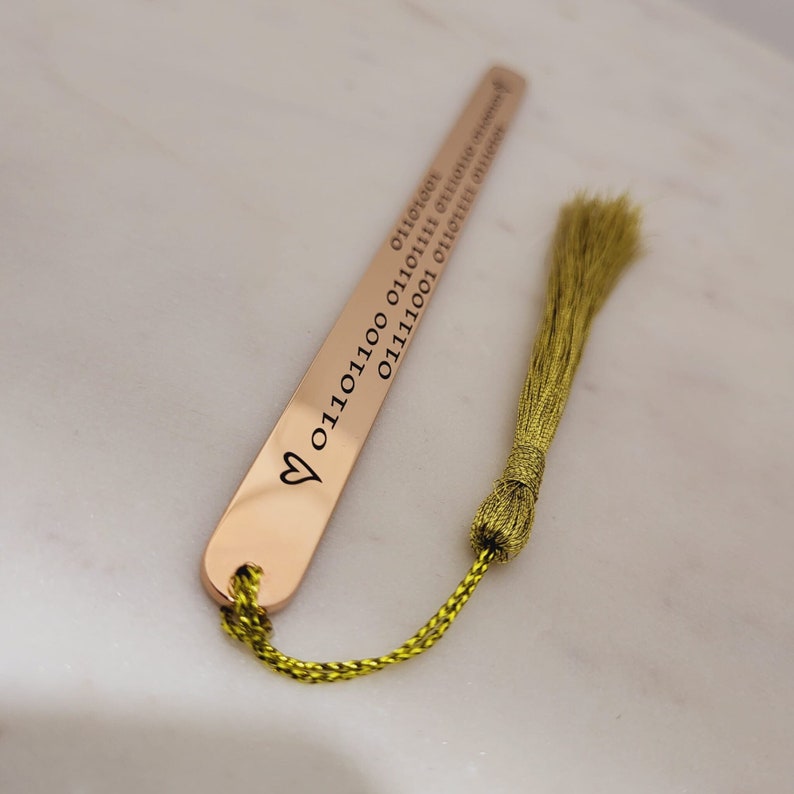 May include: A gold bookmark with a heart and the text "01111001 01101110 01100111 01110011 01110100 01100101 01110010 01110100" engraved on it. The bookmark has a green tassel.