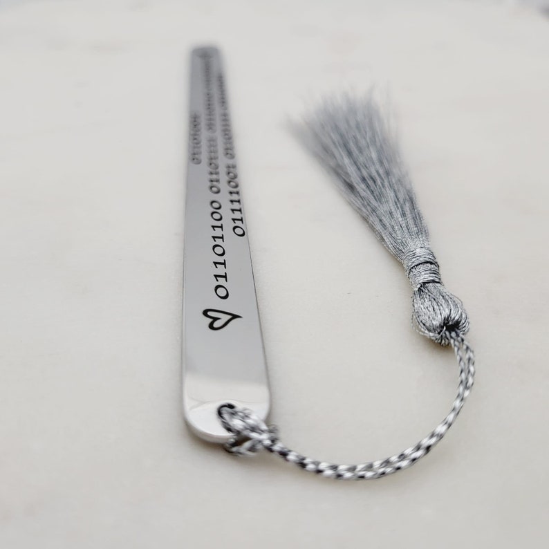 May include: Silver bookmark with a heart and a string of binary code. The bookmark has a silver tassel.