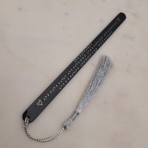 May include: A black bookmark with a silver tassel. The bookmark is engraved with a heart and a series of 0s and 1s.