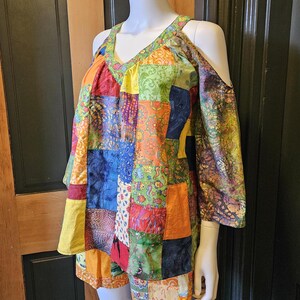 May include: A patchwork cold shoulder top with a V-neck and short sleeves. The top is made of different colored fabrics with floral and geometric patterns.