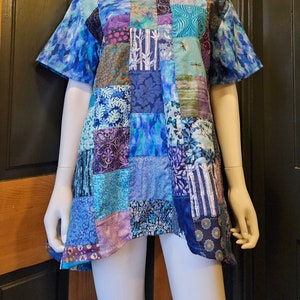 May include: A blue and purple patchwork tunic top with a square neckline and short sleeves. The top is made of various fabrics with different patterns, including floral, geometric, and abstract designs.