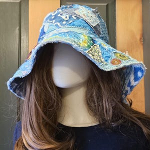 May include: A bucket hat constructed from various blue fabric patches featuring diverse patterns, including floral and geometric designs. The hat has a wide, frayed brim and is assembled with visible stitching, creating a textured, layered appearance.