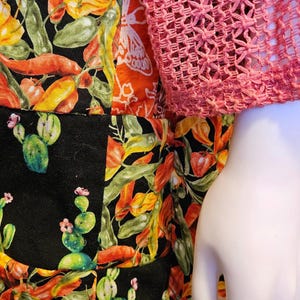 May include: A patchwork garment featuring a black fabric base with a vibrant print of orange and yellow chili peppers and green cactus plants, paired with a long-sleeved pink crocheted top with an open-weave texture.