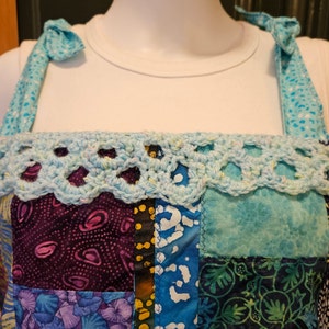 May include: A patchwork sleeveless top with a crocheted trim. The top is made of various blue and purple fabrics with floral and geometric patterns.