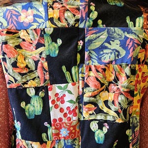 May include: A patchwork vest featuring a variety of fabric squares with prints of green cacti, red cherries, and colorful chili peppers on black and blue backgrounds. The vest is worn with a multi-colored patchwork bucket hat.