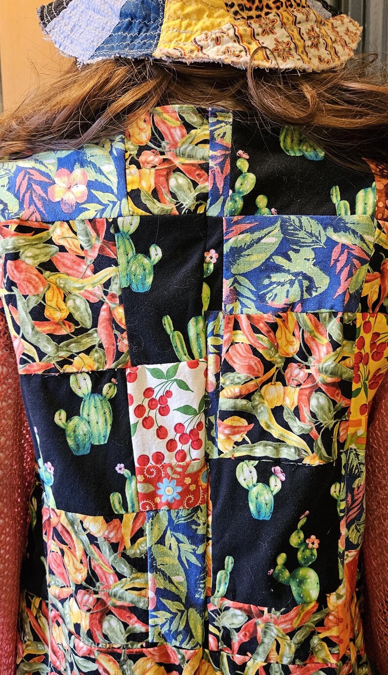 May include: A patchwork vest featuring a variety of fabric squares with prints of green cacti, red cherries, and colorful chili peppers on black and blue backgrounds. The vest is worn with a multi-colored patchwork bucket hat.
