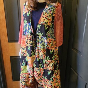 May include: A patchwork duster featuring a black base with a colorful cactus print, long sleeves with a textured coral-colored mesh fabric, and a front tie closure. The outfit includes a matching patchwork bucket hat and wide-leg patchwork trousers.