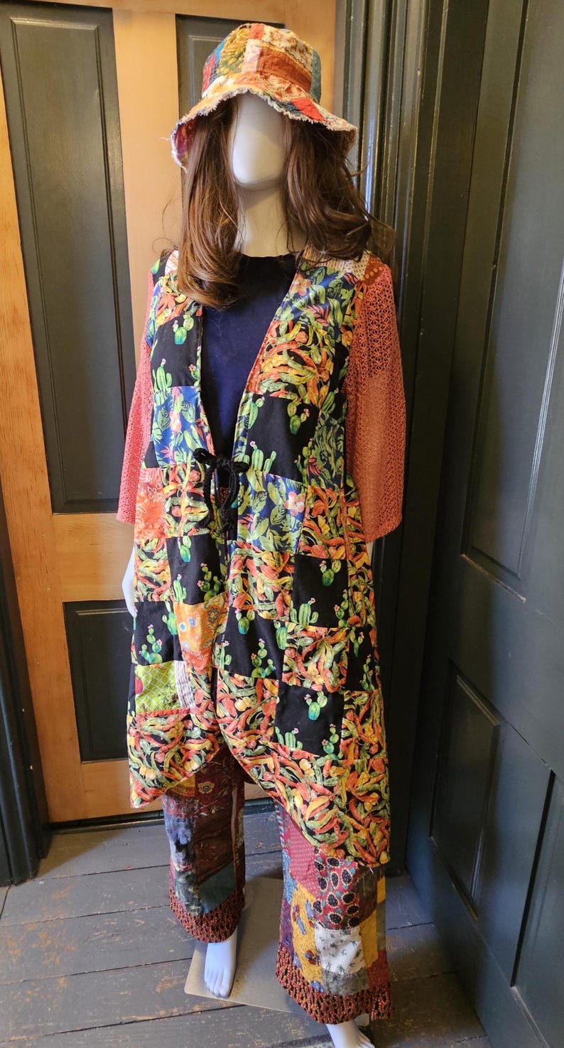 May include: A patchwork duster featuring a black base with a colorful cactus print, long sleeves with a textured coral-colored mesh fabric, and a front tie closure. The outfit includes a matching patchwork bucket hat and wide-leg patchwork trousers.