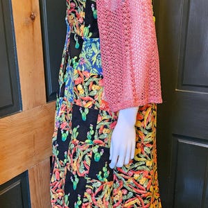 May include: A sleeveless dress featuring a patchwork design with black squares and vibrant, multi-colored botanical prints of cacti and chili peppers, complemented by a separate, textured, dusty pink, open-knit, three-quarter sleeve bolero.