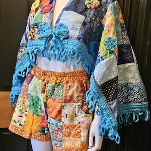 May include: A patchwork crochet top with blue fringe and floral embellishments. The top is paired with patchwork shorts in a variety of colors and patterns.