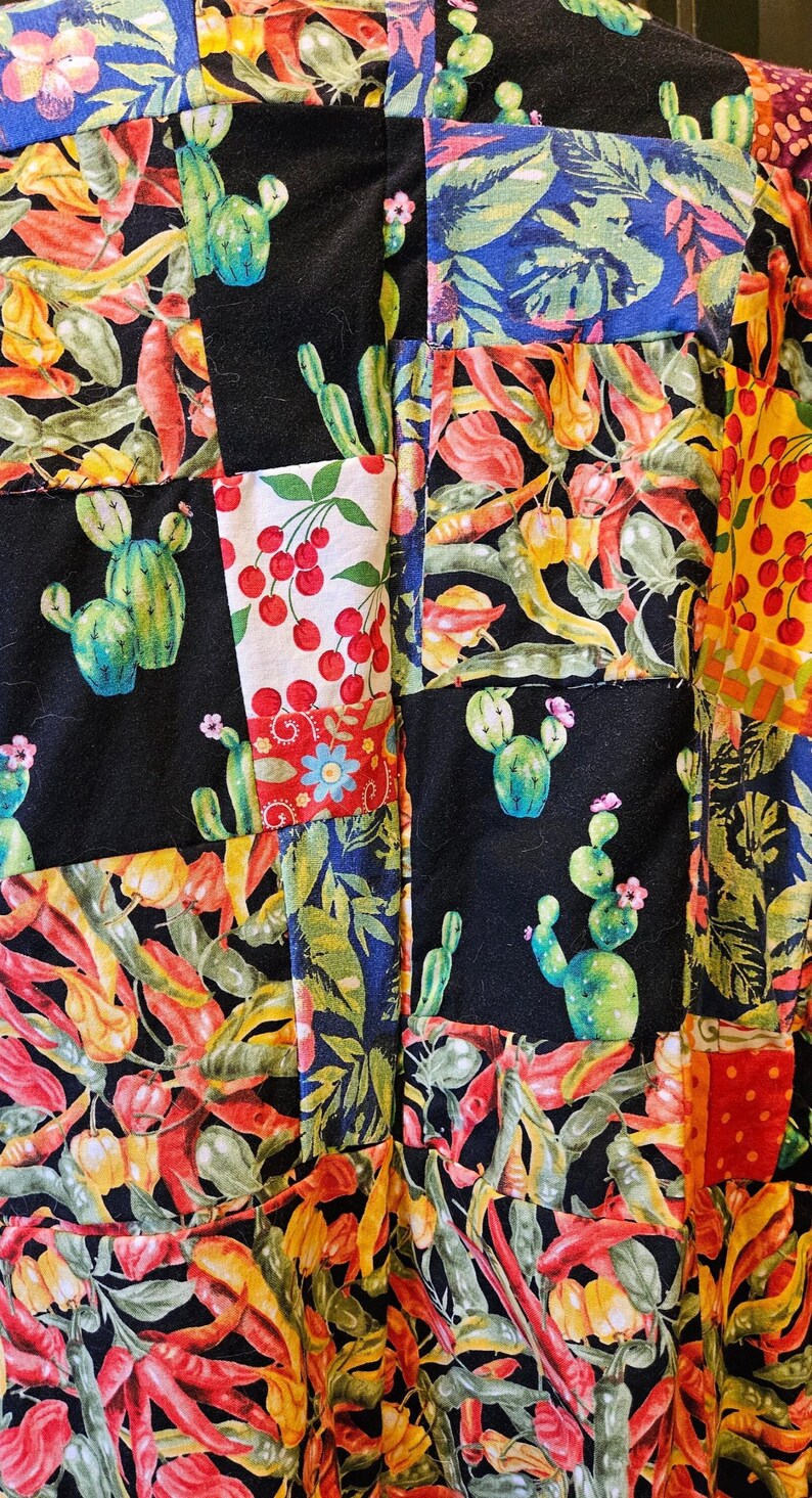 May include: A patchwork fabric featuring a variety of square panels with colorful prints. The patterns include green cacti, red cherries, yellow and red chili peppers, and lush green tropical leaves set against black and white backgrounds.