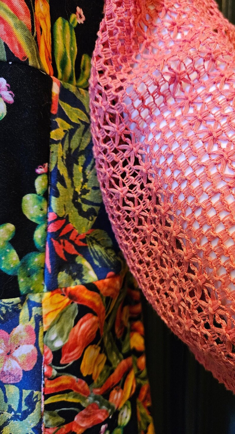 May include: A garment featuring a black base fabric with a vibrant, multi-colored botanical print of green cacti, orange peppers, and pink flowers, paired with a textured, open-weave coral-colored crochet overlay piece.
