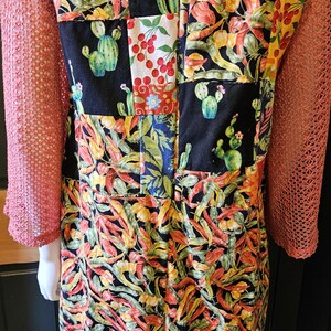 May include: A garment featuring a patchwork design of black fabric squares printed with green cacti and red cherries, interspersed with sections of vibrant chili pepper patterns. The sleeves are made of a textured, coral-colored mesh fabric.