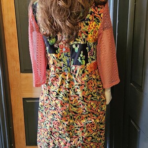 May include: A patchwork bucket hat and a long-sleeved dress featuring a vibrant cactus and chili pepper print. The dress has coral-colored mesh sleeves and is paired with patchwork trousers in various patterns and colors, including yellow and brown.