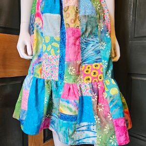 Puede incluir: Una falda de patchwork con una mezcla de patrones florales, geométricos y abstractos en tonos de azul, rosa, verde y amarillo. La falda tiene un diseño de capas y una cintura elástica.