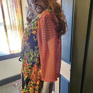May include: A patchwork bucket hat with a multi-colored floral and geometric pattern paired with a dress featuring a black base with vibrant tropical leaf prints and three-quarter length sleeves made of a coral-colored openwork crochet fabric.