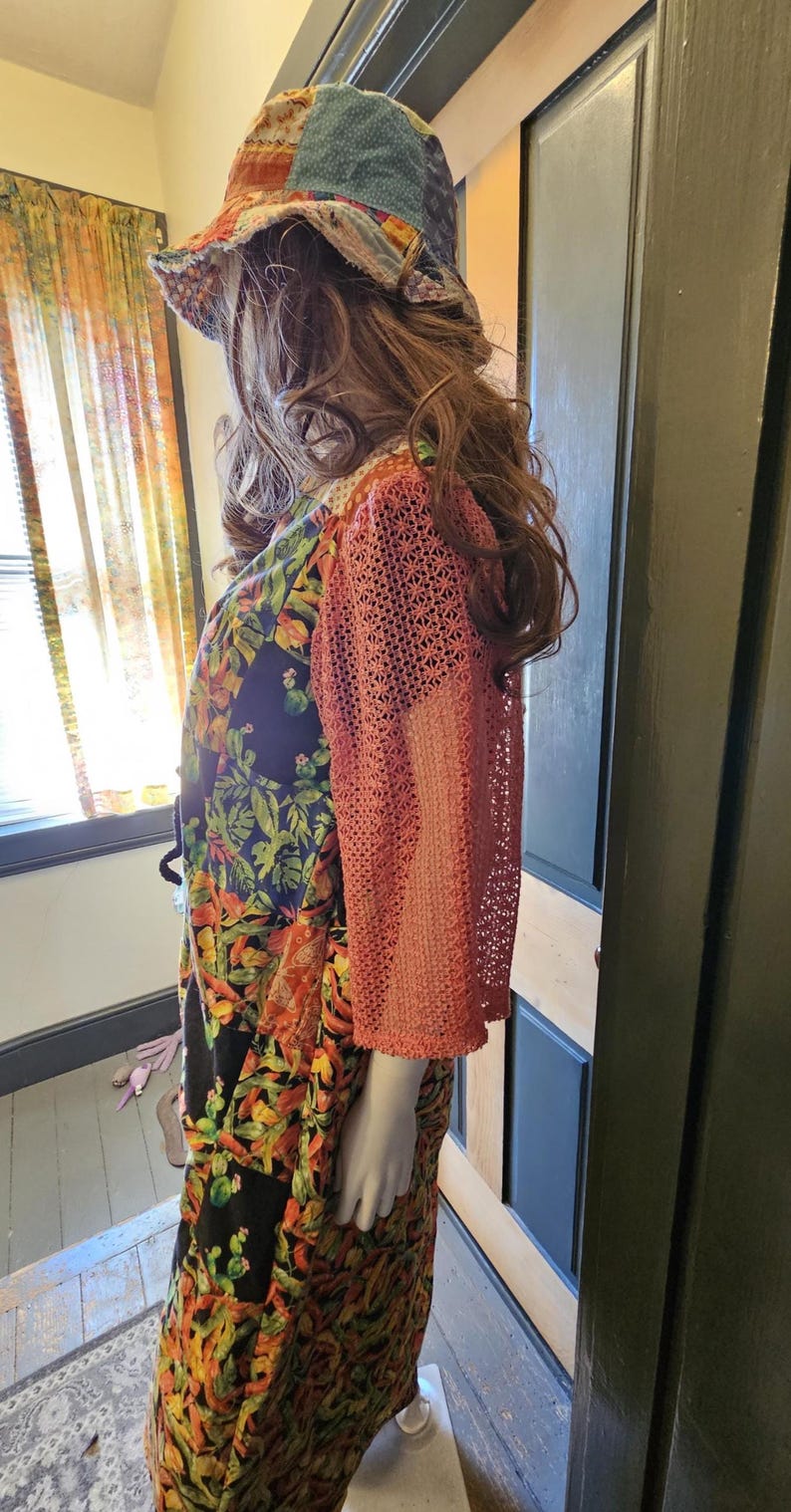 May include: A patchwork bucket hat with a multi-colored floral and geometric pattern paired with a dress featuring a black base with vibrant tropical leaf prints and three-quarter length sleeves made of a coral-colored openwork crochet fabric.