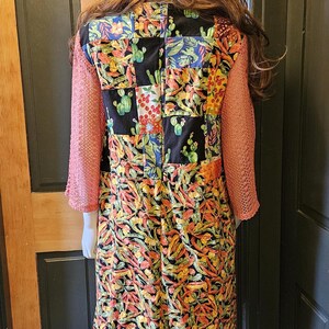 May include: A patchwork bucket hat and a long-sleeved dress featuring a black background with a colorful cactus and chili pepper print. The dress has textured, salmon-colored sleeves and a multi-patterned patchwork bodice section.