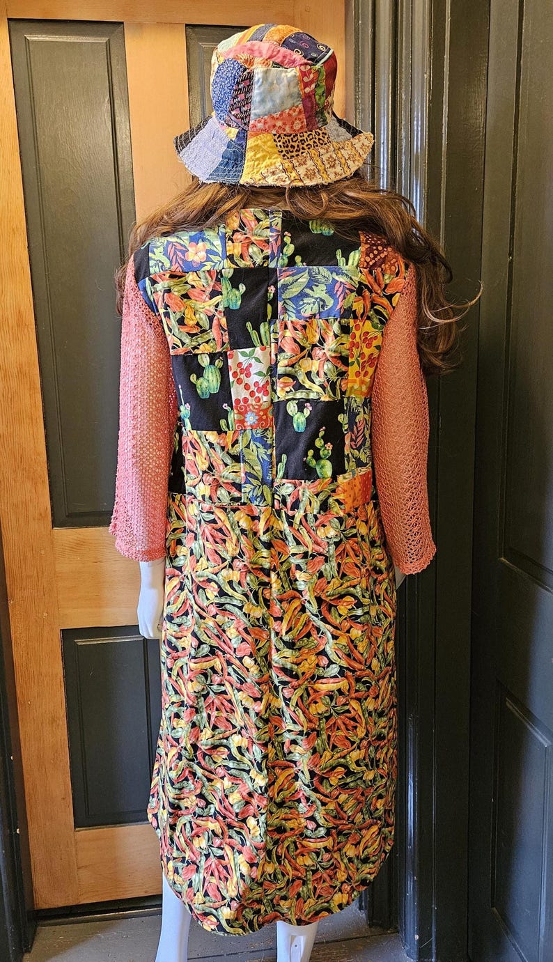 May include: A patchwork bucket hat and a long-sleeved dress featuring a black background with a colorful cactus and chili pepper print. The dress has textured, salmon-colored sleeves and a multi-patterned patchwork bodice section.