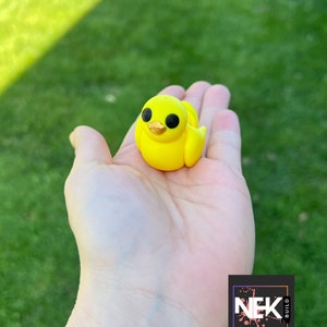 Op de afbeelding: Een klein geel rubberen eendje met zwarte ogen en een gouden snavel. Het eendje zit in de palm van een hand.