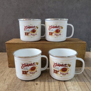 Może przedstawiać: Cztery białe emaliowane kubki z czerwoną i złotą etykietą zupy Campbell's z napisem "12¢ Tomato Soup".