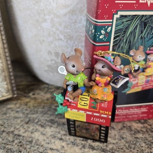 May include: A decorative Christmas ornament featuring two mouse figurines. One mouse holds a camera, the other wears a hat. The ornament is on a film strip base with the text "1996" and "For Christmas Together". A red box is in the background.