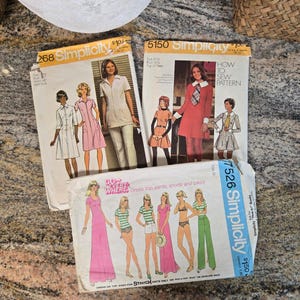 May include: Three vintage Simplicity sewing pattern envelopes. The patterns feature illustrations of dresses, tops, pants, and shorts. The envelopes are labeled with numbers and include the text "How to Sew Pattern".