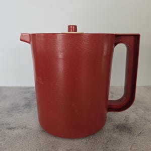 Può includere: Una caraffa di plastica rossa con un coperchio e un manico. La caraffa è realizzata in plastica testurizzata.