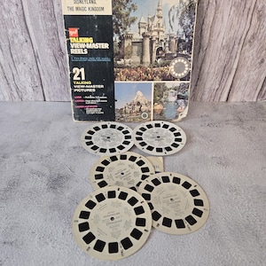 May include: A set of 21 vintage View-Master reels featuring Disneyland, The Magic Kingdom. The reels are in their original box, which features a picture of Sleeping Beauty's Castle. The reels are made of cardboard and have a black and white design.