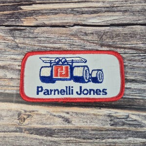 May include: Embroidered patch featuring a stylized race car design in blue and white, with a red and white logo. The text "Parnelli Jones" is displayed in blue below the car.