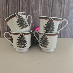 May include: Set of four white ceramic Christmas tree mugs with green, red and white trim. Each mug features a green Christmas tree with decorations and a red ribbon.