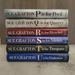 May include: A stack of six hardcover books by Sue Grafton, each with a different colored cover and featuring a letter of the alphabet and the title "is for..."  The books are part of the "Kinsey Millhone" mystery series.  The titles are "P is for Peril", "Q is for Quarry", "R is for Ricochet", "S is for Silence", "T is for Trespass", and "U is for Undertow".