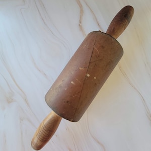 May include: A vintage wooden rolling pin with a brown wooden handle. The rolling pin has a worn, rustic look and is perfect for baking.