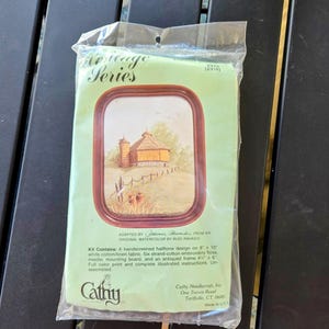 Peut inclure: Un kit de point de croix représentant une ferme rustique avec un toit rouge et un champ vert. Le kit comprend un tissu imprimé, du fil à broder, une aiguille, un support de montage et un cadre antique. Le kit est de Cathy Needlecraft, Inc. et est fabriqué aux États-Unis.