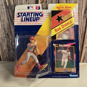 Peut inclure: Un objet de collection sportive Starting Lineup avec une figurine de joueur de baseball en uniforme gris et rouge. L'emballage comprend un ensemble d'affiches et une carte de baseball de Rob Dibble. L'emballage indique "Starting Lineup" et "Sports Super Star Collectibles."