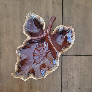 May include: A brown and white ceramic leaf-shaped serving dish with a glossy finish. The dish has a three-dimensional design and is ideal for serving snacks or appetizers.