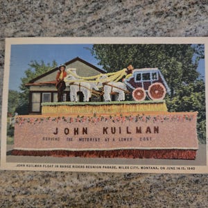 Op de afbeelding: Vintage ansichtkaart met een parade-optocht met een huis, paarden en een koets. De praalwagen heeft de tekst "JOHN KUILMAN SERVING THE MOTORIST AT A LOWER COST". De ansichtkaart is van de Range Riders Reunion Parade in Miles City, Montana, gedateerd 14-15 juni 1940.