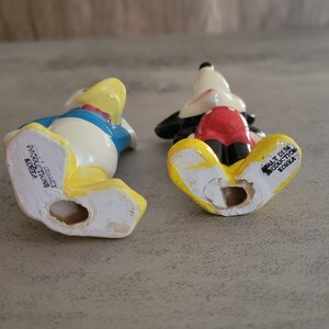 Op de afbeelding: Onderkant van twee keramische beeldjes, een van Mickey Mouse en een van Donald Duck. Beide beeldjes zijn geel, wit, rood en blauw. Het Mickey Mouse beeldje heeft de tekst "Walt Disney Productions Korea" op de onderkant. Het Donald Duck beeldje heeft de tekst "Walt Disney Productions Korea" op de onderkant.