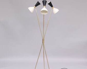May include: A gold tripod floor lamp with three black and white cone-shaped shades. The lamp has a black cord and a black plug.
