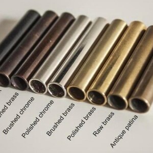 Pu&ograve; includere: Primo piano di otto tubi metallici in diverse finiture: nero opaco, nero antico, ottone annerito, cromo spazzolato, cromo lucido, ottone spazzolato, ottone lucido, ottone grezzo e patina antica.