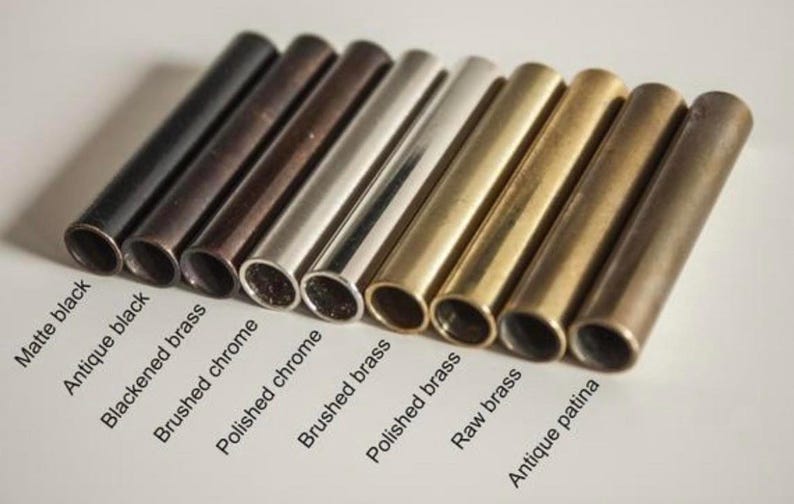 Pu&ograve; includere: Primo piano di otto tubi metallici in diverse finiture: nero opaco, nero antico, ottone annerito, cromo spazzolato, cromo lucido, ottone spazzolato, ottone lucido, ottone grezzo e patina antica.