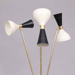 Pu&ograve; includere: Una lampada da terra in ottone con tre bracci regolabili e paralumi a forma di cono neri e bianchi. La lampada ha un design moderno di met&agrave; secolo.
