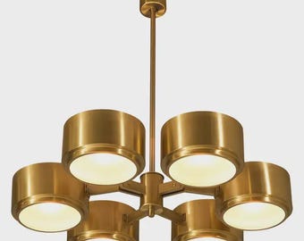 May include: A brass-colored chandelier with six cylindrical light fixtures. The light fixtures are arranged around a central hub and are suspended from a central rod. The light fixtures have a warm, inviting glow.