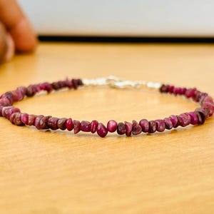 Puede incluir: Un delicado brazalete hecho con pequeñas cuentas de rubí irregulares. El brazalete está enhebrado en una cadena de plata.