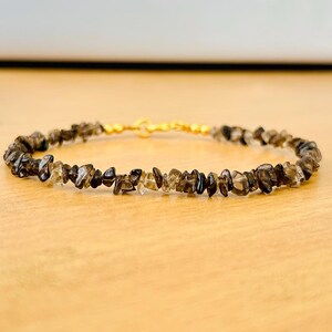 May include: A delicate bracelet made with small, irregular pieces of smoky quartz, strung on a gold-toned wire.